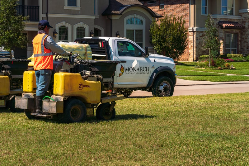 lawn care team fertilizes lawn at home with truck full of fertilizer in background